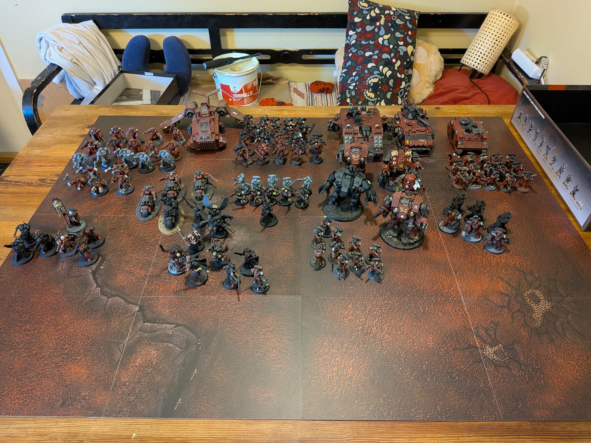 a photo of a table, half covered in small plastic toy soldiers of the Warhammer variety. most of them are painted red and black, but some are still grey.