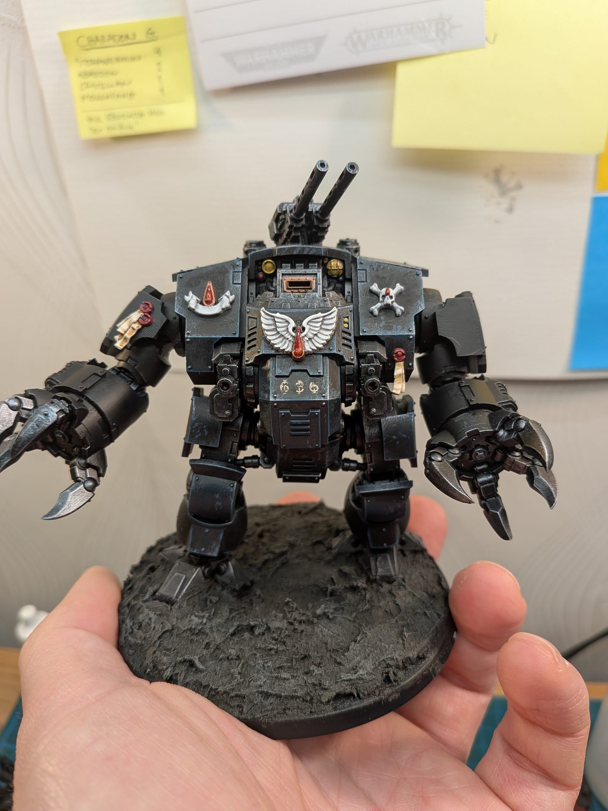 A photo of a modern Dreadnought for Warhammer 40 000. It is a robot-looking thing, boxy and brutal, mostly black, with big ole claws on its arms.